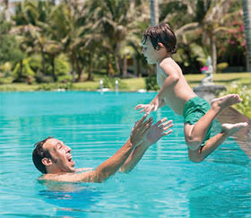 boy jumping into the pool with dad waiting to catch him