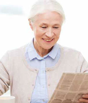 elderly woman smiling and reading newspaper