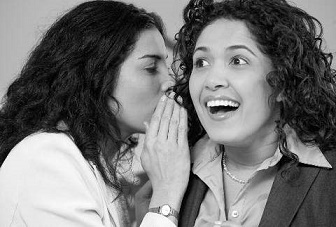 woman whispering into another woman's ear